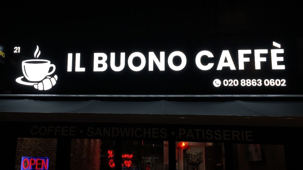 The same Il Buono Caffè shop front at night with the letters and cup logo lit