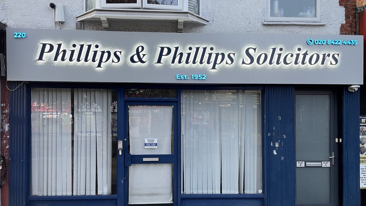 The same Phillips & Phillips shop front at night, the letters glowing with a white halo