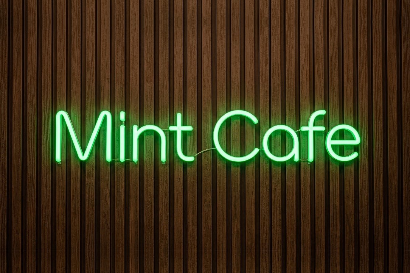 Green neon-effect script reading Mint Cafe on a walnut fluted wall